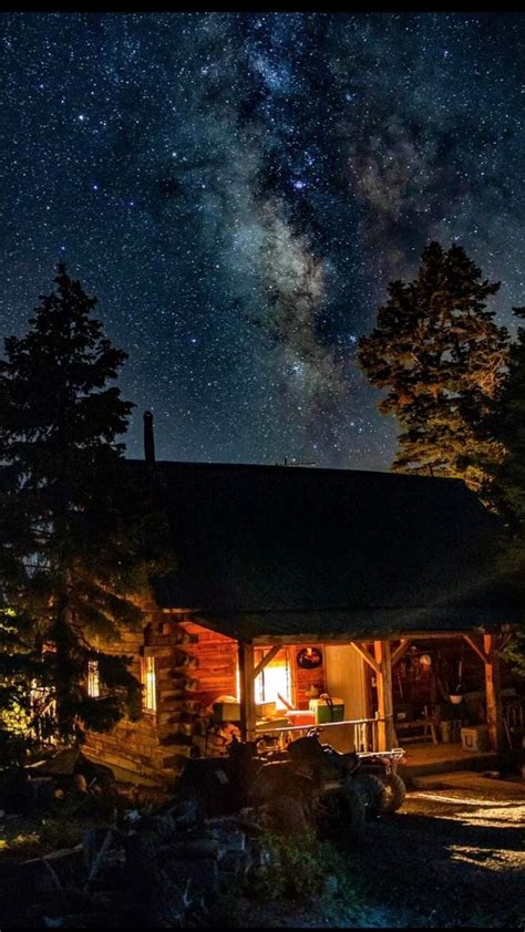 the night sky is filled with stars above a log cabin and tree lined ...