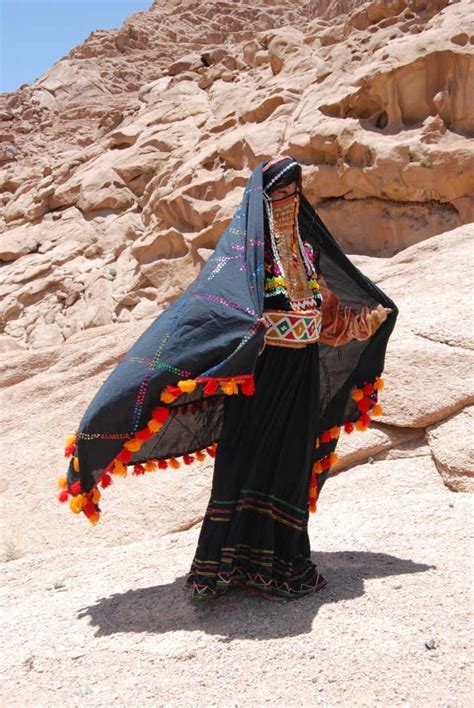 a woman in black dress standing on top of a rocky hill next to a mountain