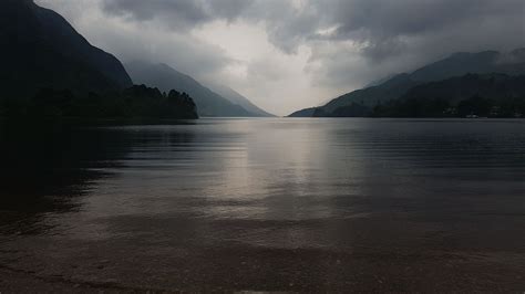 a lake with mountains in the background under a cloudy sky and dark ...