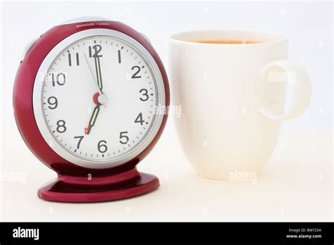 Mug of tea by a red alarm clock at 7 am in the morning just seconds ...