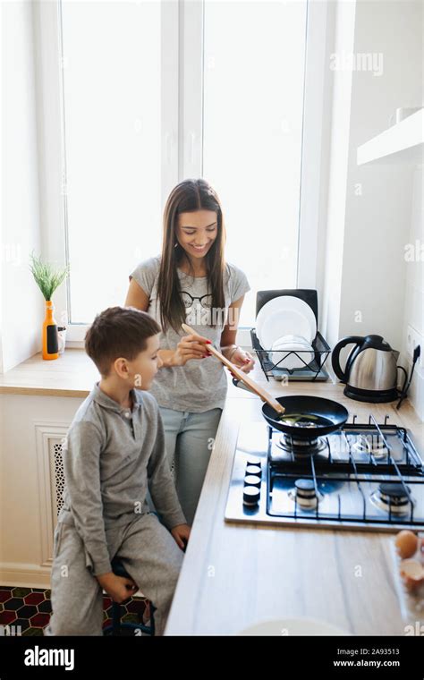 Cute little boy and his mom smiling and cooking in kitchen at home ...