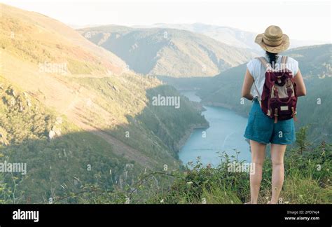 Young girl with backpack and hat observes mountainous landscape with ...