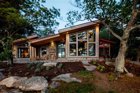 a house with large windows sitting on top of a hill next to rocks and trees