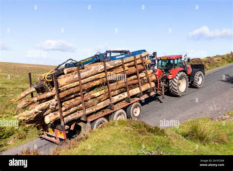 A tractor towing a trailer with a heavy load of logs up a hill on ...