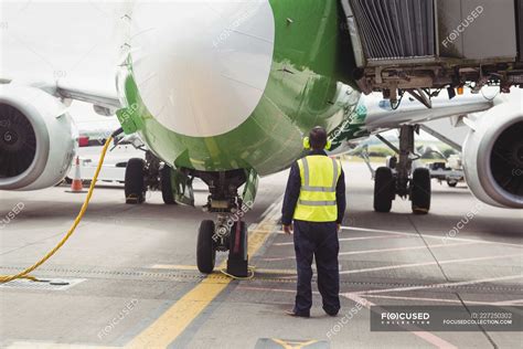 Rear view of airport ground crew worker directing airplane on runway ...