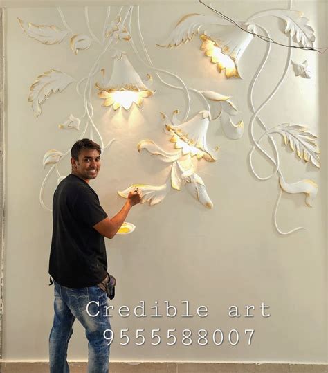 a man standing in front of a white wall with flowers on it and lights ...