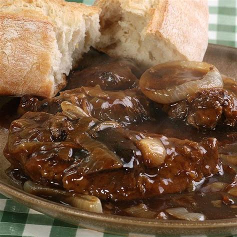 a plate with meat and mushrooms covered in gravy next to bread on a ...