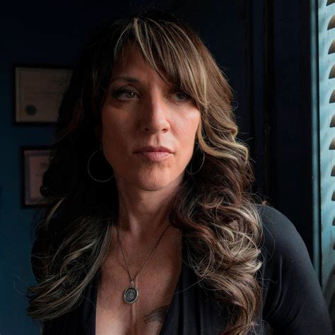 a woman with long hair wearing a black shirt and necklace looking off ...