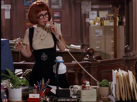 a woman with red hair and glasses standing in front of a desk holding a ...