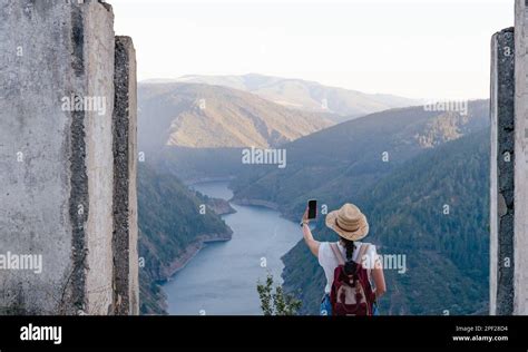 Woman with backpack and hat taking selfie in mountainous landscape ...