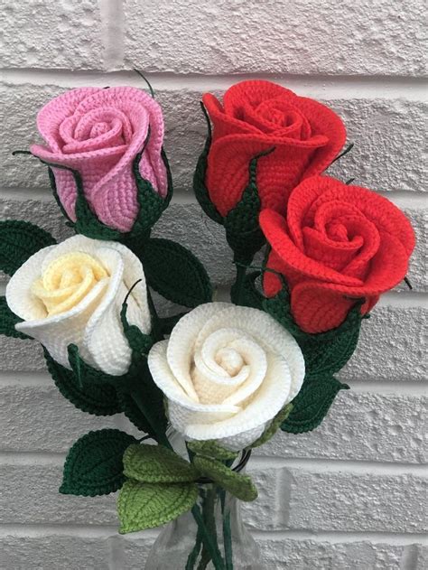 three crocheted roses in a glass vase on a brick wall with green leaves