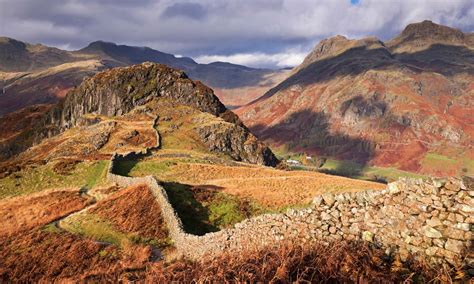 a stone wall in the middle of mountains with grass and rocks on each ...