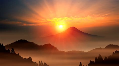 the sun is setting over mountains with trees in the foreground and fog ...