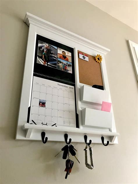 a white wall mounted shelf with two magnets and a calendar hanging on ...