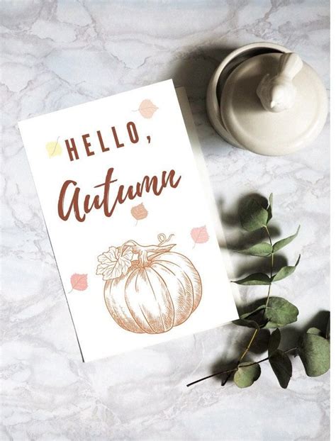 a hello autumn card next to some leaves and a teapot on a marble surface