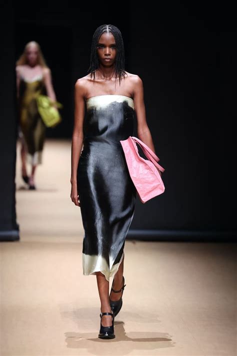 a woman in a black and white dress walking down the runway with a pink ...