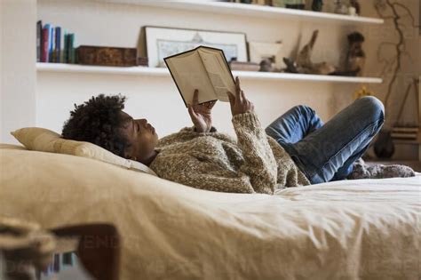 Young woman lying on bed reading a book stock photo