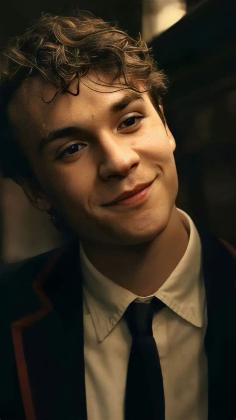 a young man with curly hair wearing a suit and tie, smiling at the camera