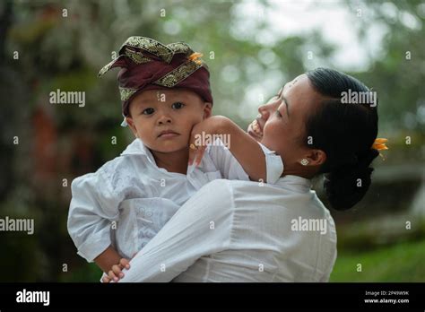 Boy wearing udeng (headress) in smiling mother's arms during Mepeed ...