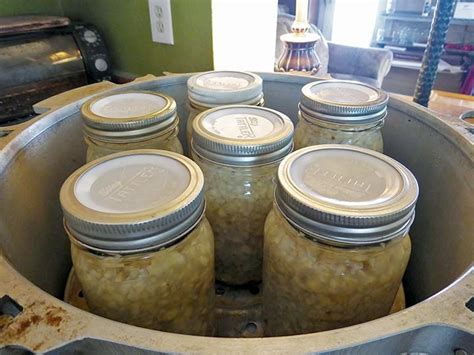 six jars filled with pickles sitting in a metal container on top of a table