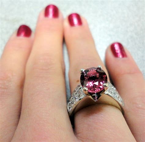 a close up of a person's hand wearing a ring with a pink diamond