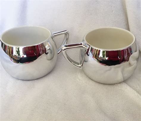 two shiny metal cups sitting next to each other on a white cloth ...