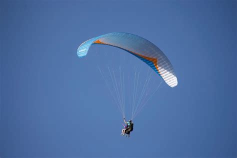 Faceless person flying paraglider over green countryside · Free Stock Photo