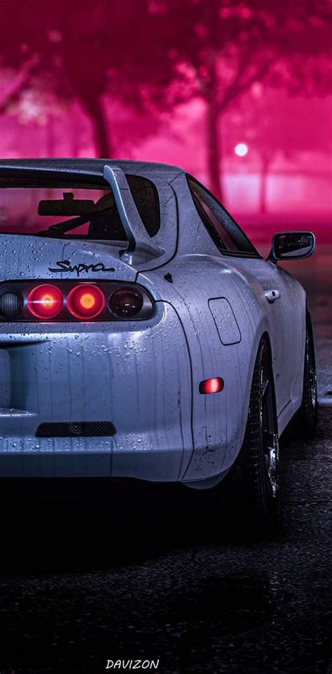 the back end of a white sports car parked in front of a red light at night