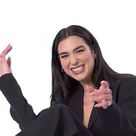 a woman in a black suit is smiling and holding her hand up to the side