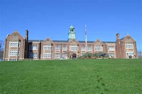 an old brick building with a clock tower on the top and green grass in ...