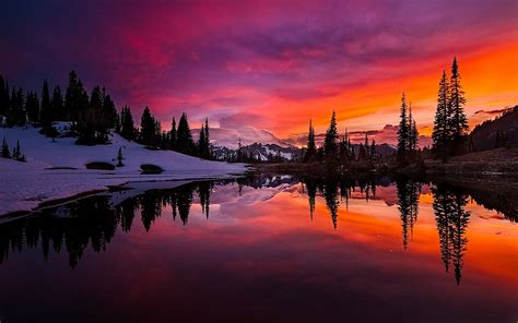 Three beside calm body water across snow covered mountain during golden ...