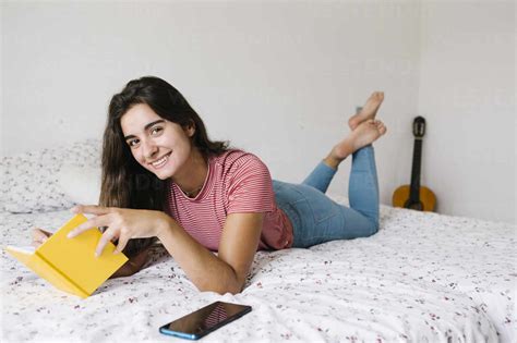 Young woman reading book while lying down on bed at home stock photo