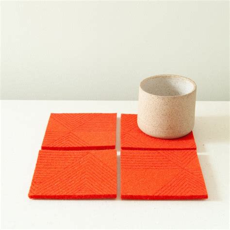 two orange coasters sitting on top of a white table next to a cup and ...