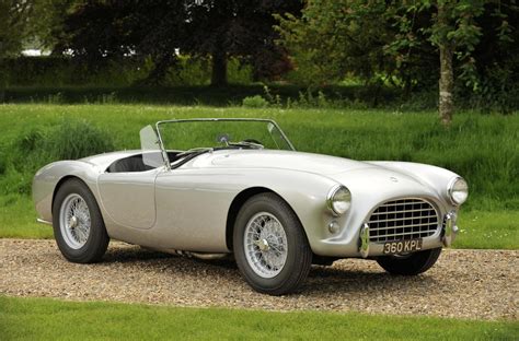 an old silver sports car is parked on the gravel