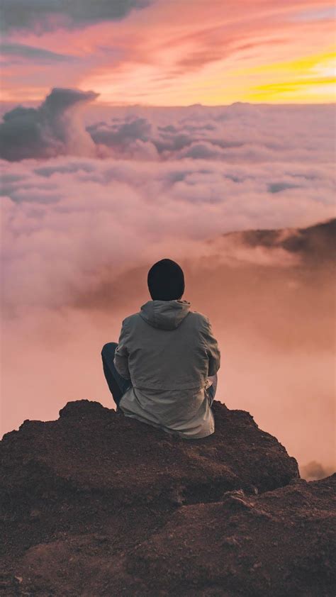 a man sitting on top of a mountain looking at the clouds