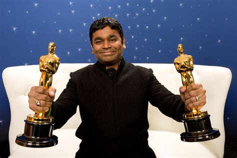 a man sitting on a couch holding two oscar statues