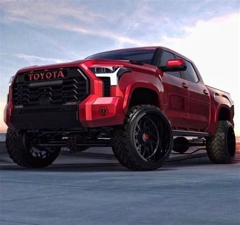 a red truck parked on top of a parking lot next to the ocean at sunset