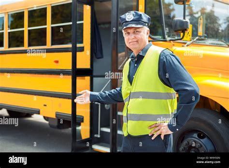 Senior driver weaering uniform standing near school bus showing door ...