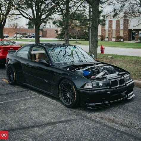 a black car parked in a parking lot next to some trees and buildings ...