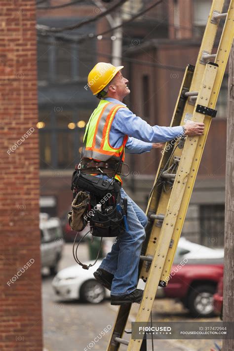 Cable lineman climbing up a ladder on city building — Tool Belt, on the ...