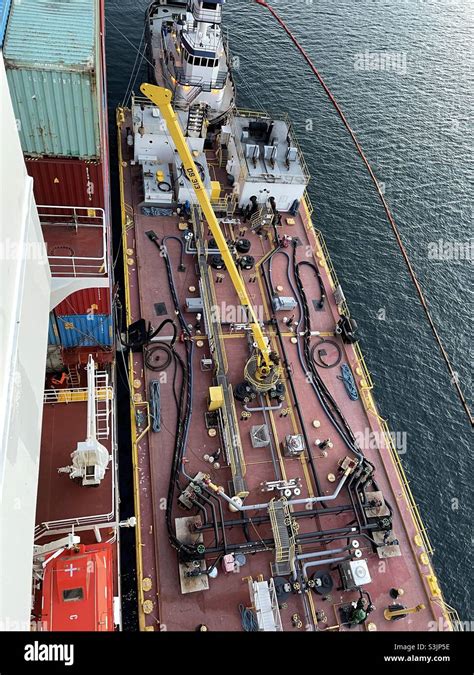 Bunker barge with white tugboat alongside merchant container vessel ...