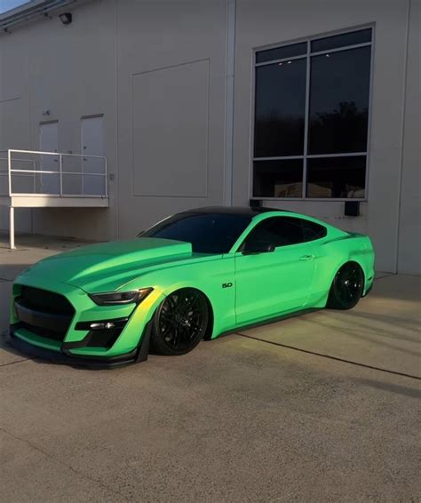 a bright green mustang parked in front of a white building with black ...