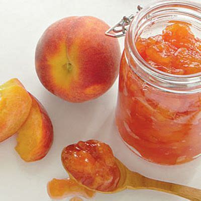 peach jam in a glass jar with a wooden spoon next to it and two sliced ...