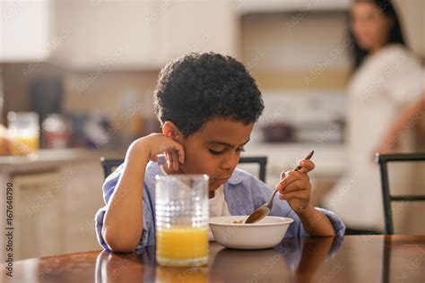 cute little boy eating breakfast with mother behind him Stock Photo ...