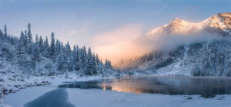 Sunrise in winter mountains. Mountain reflected in ice lake in morning ...