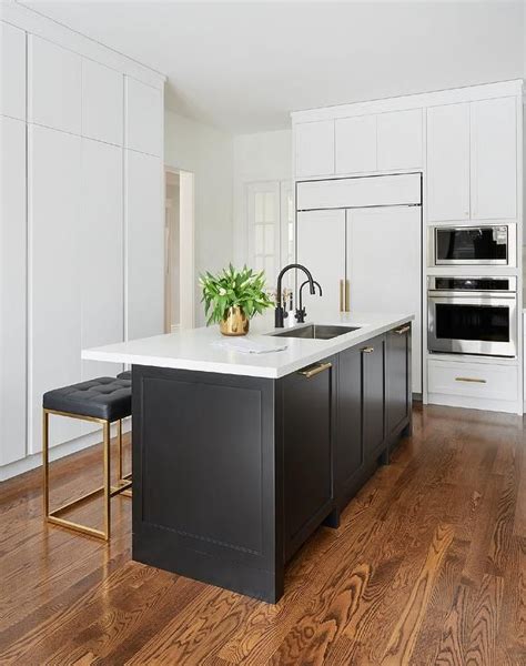 Chic white and black kitchen boasts a black shaker island accented with ...