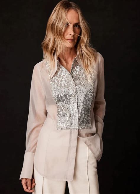 a woman wearing a white suit and silver sequins on her shirt is ...