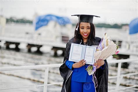 African american student girl in black graduation gown with diploma, at ...