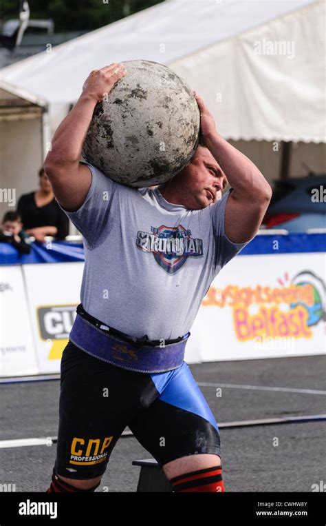 Man competing in a strongman contest lifts a very heavy Atlas Stone ...