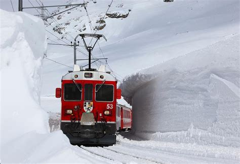 a red and white train traveling down tracks in the snow next to a ...